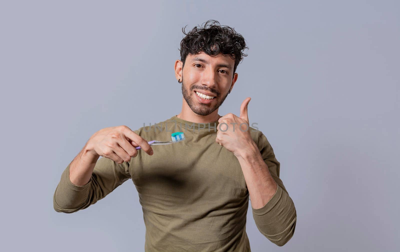 Young man holding a toothbrush with thumb up isolated. Smiling handsome guy holding a toothbrush with thumb up. Smiling people holding toothbrush with thumbs up gesture by isaiphoto
