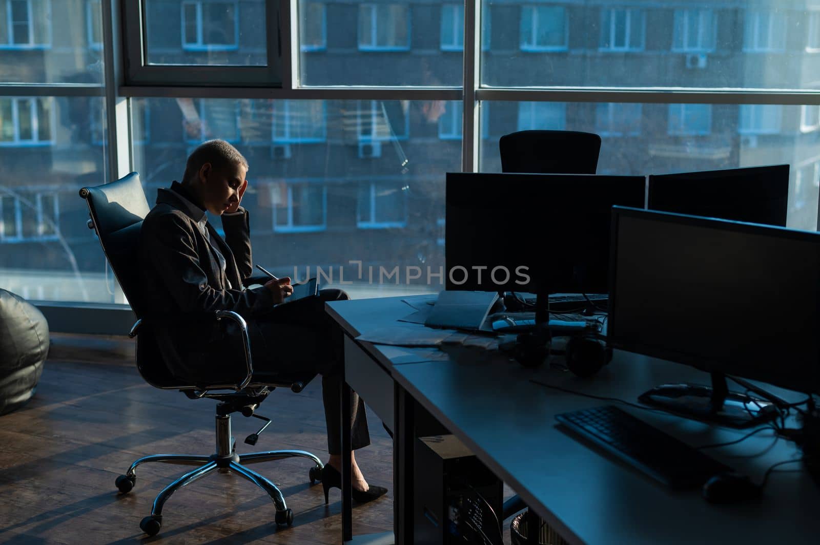 Business woman with short hair sits by the window and writes on a digital tablet with a stylus pen.