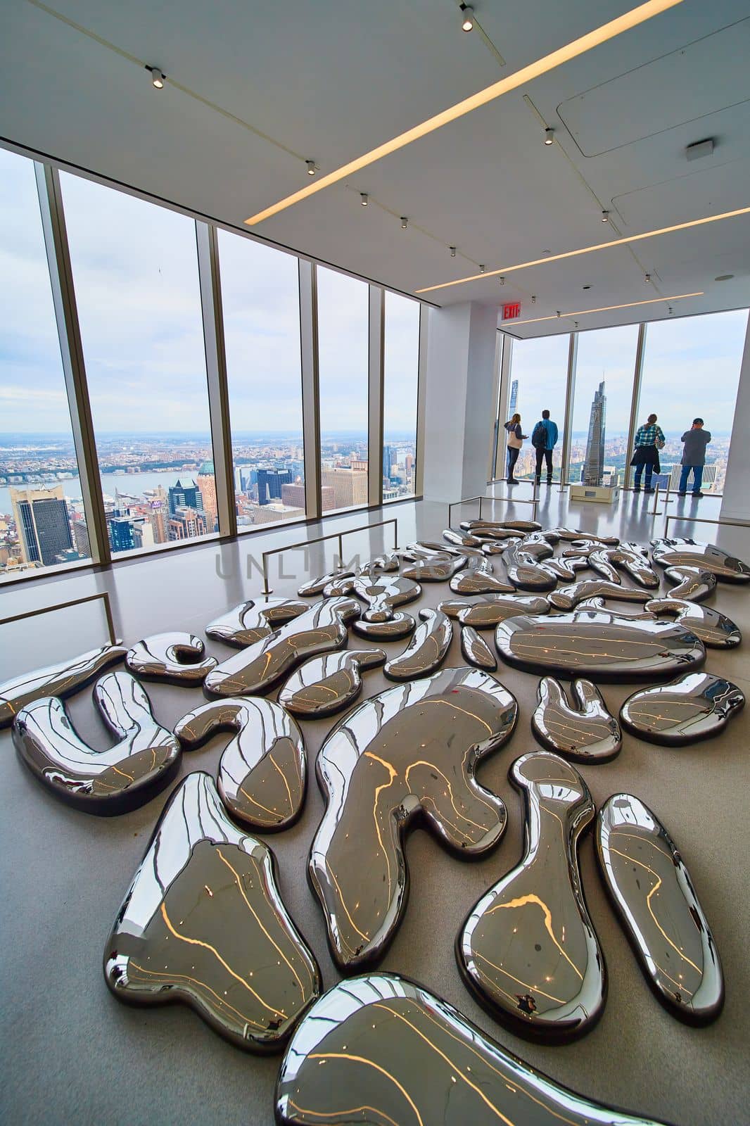 Image of Mirror metal melted abstract shapes cover ground in exhibit overlooking New York City from above