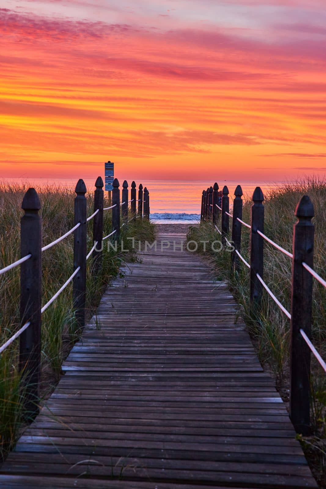 Image of Orange and red sunrise light with straight boardwalk path guiding you to beach