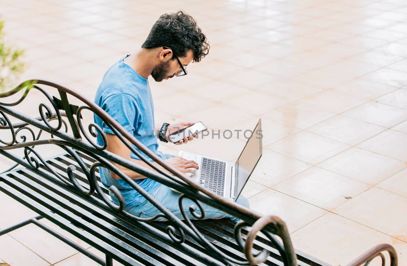Entrepreneur man working with laptop and cellphone in a park. Freelance man working with laptop while using phone, young man sitting in a park working with his laptop and cell phone