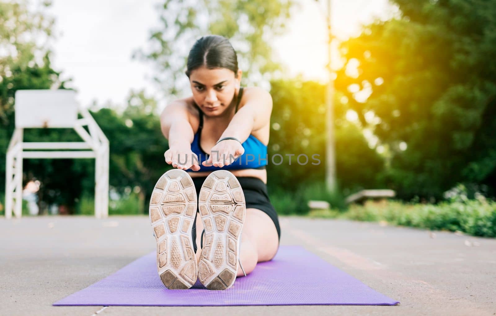 Athlete woman sitting doing leg stretch in a park. Athlete girl sitting on a mat stretching her legs in a park, Sporty girl stretching her legs sitting on a mat in a park
