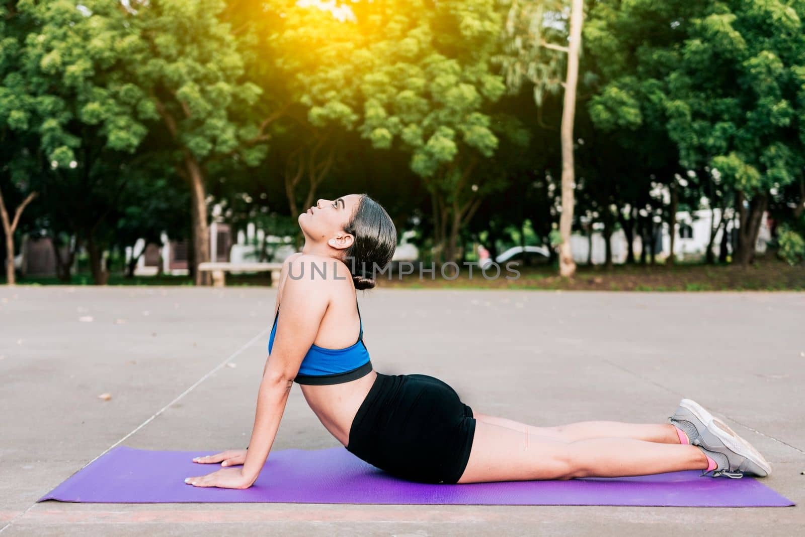 Sporty woman stretching her body doing cobra pose in a park. Athlete woman doing cobra pose in a park. Athlete woman doing yoga Bhujangasana in a park