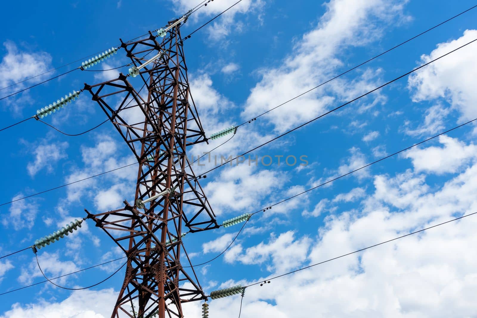 A pole of a high-voltage electric line on the background of a blue sky with white clouds