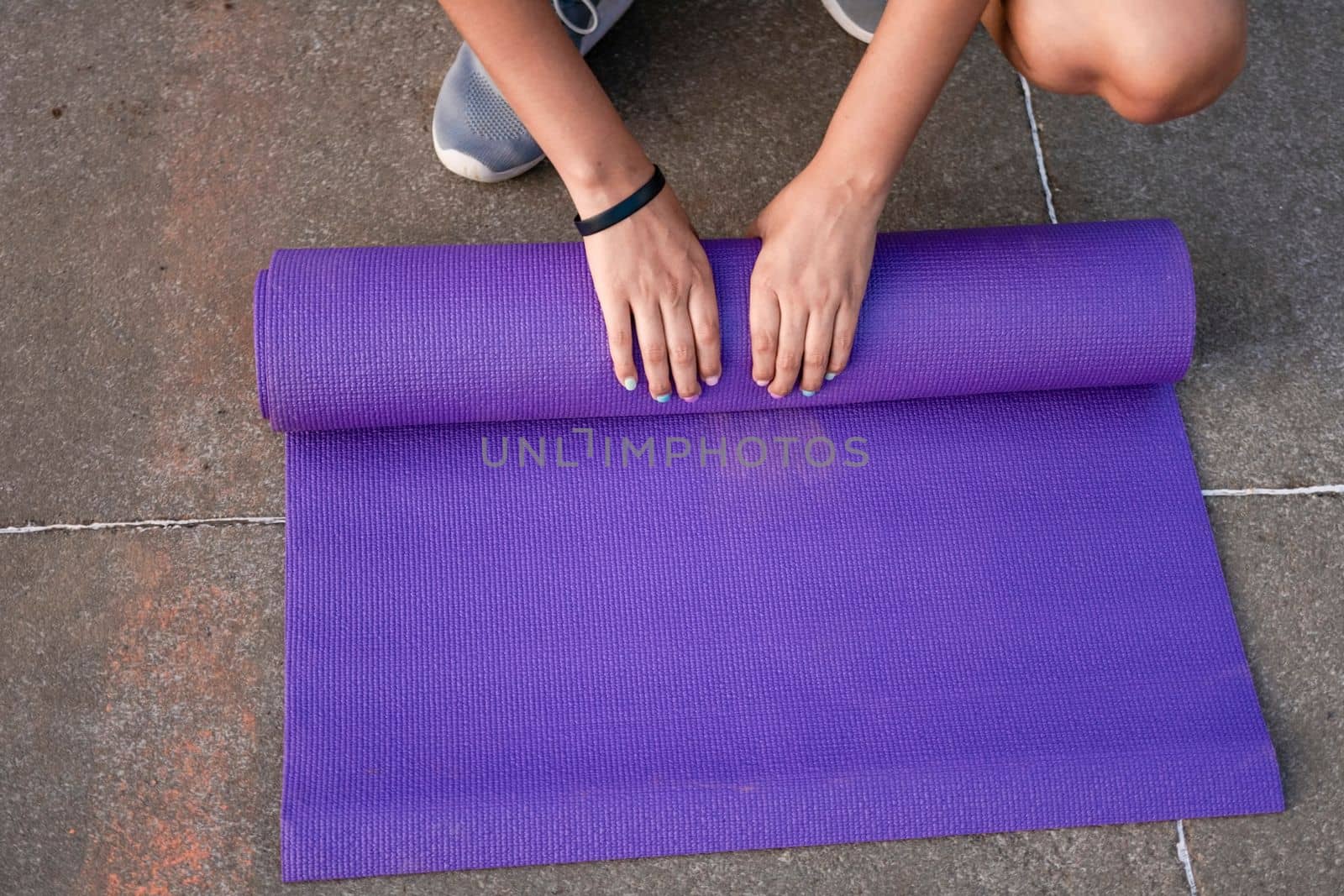 Woman hands rolling up the mat outside. Athlete woman's hands rolling up the mat after exercising. Concept of rolling up mat after exercise