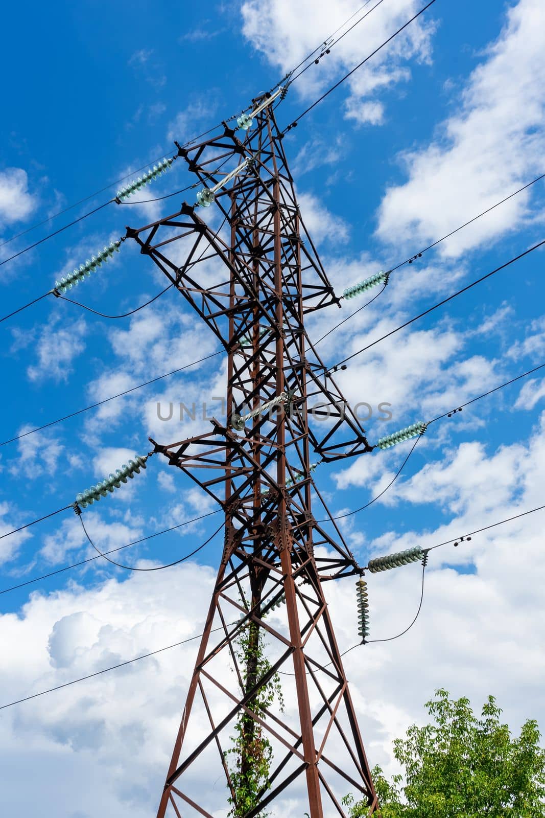 A pole of a high-voltage electric line on the background of a blue sky with white clouds.