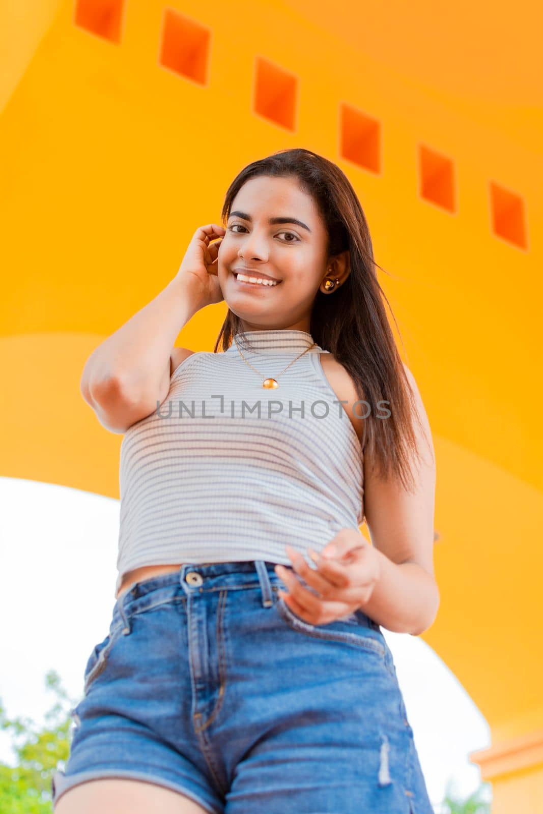 Portrait of attractive Latin girl outdoors. Smiling latin young woman looking at camera outdoors. Low angle of a cute and smiling Latin girl outdoors. Latin people portrait concept