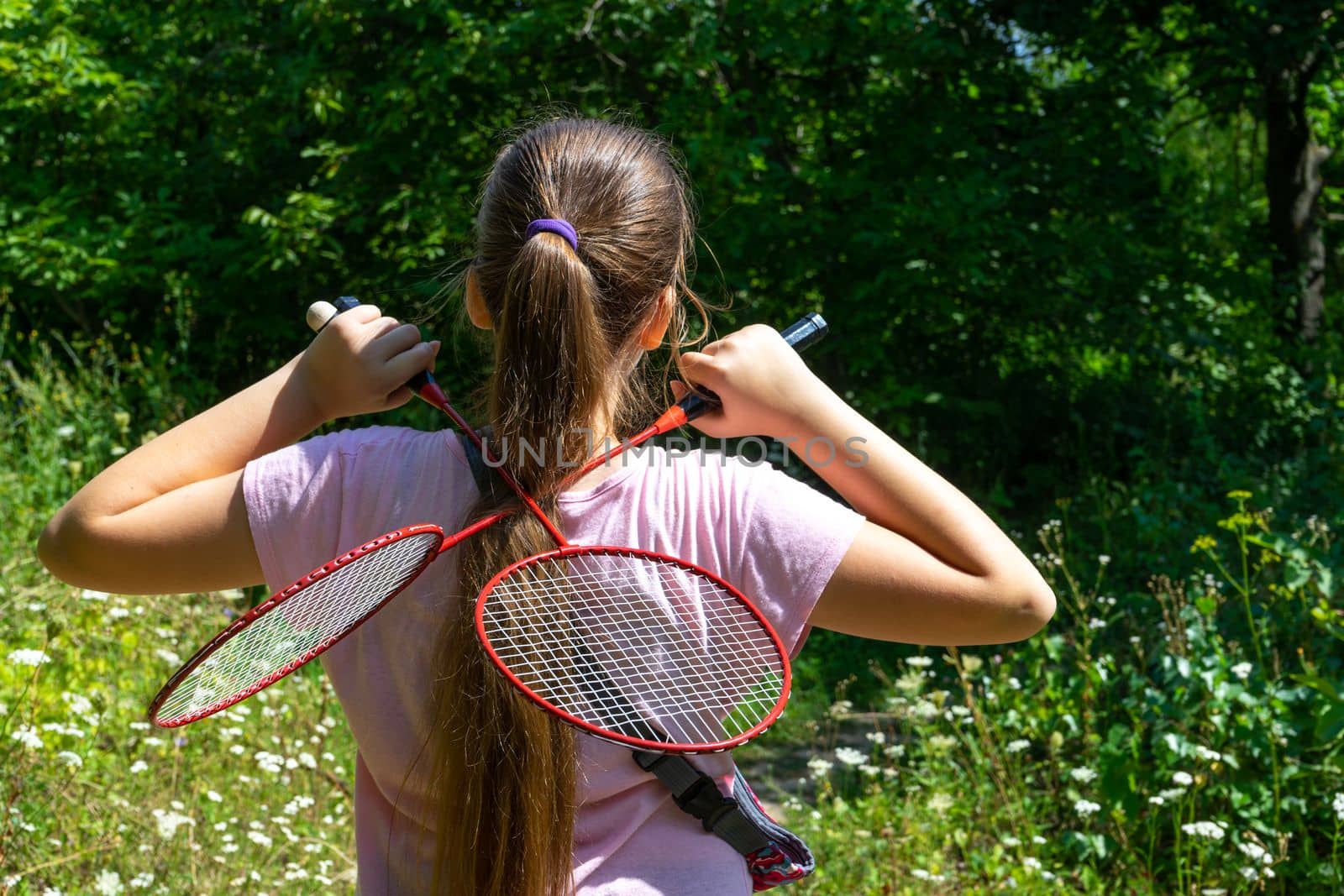 A girl stands in a forest clearing with two tennis rackets crossed on her back.