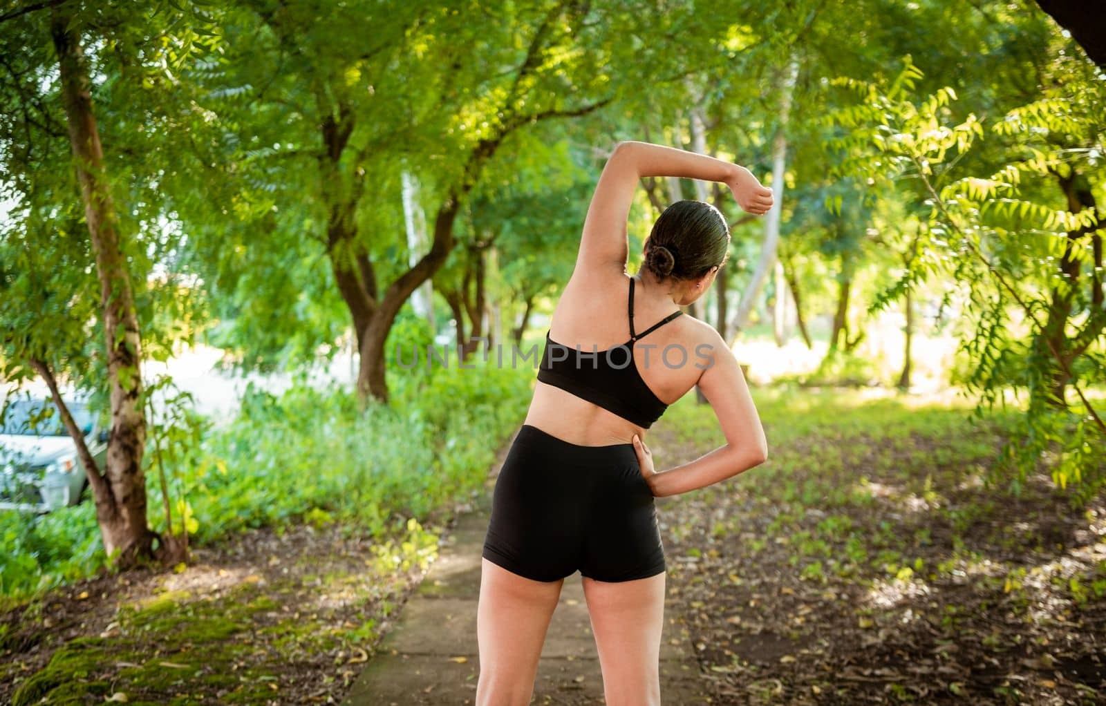 Athlete girl doing warm-up exercises in a park. Sporty woman doing stretching exercises before running. Athlete girl stretching arms before running. Concept of physical activity and healthy life