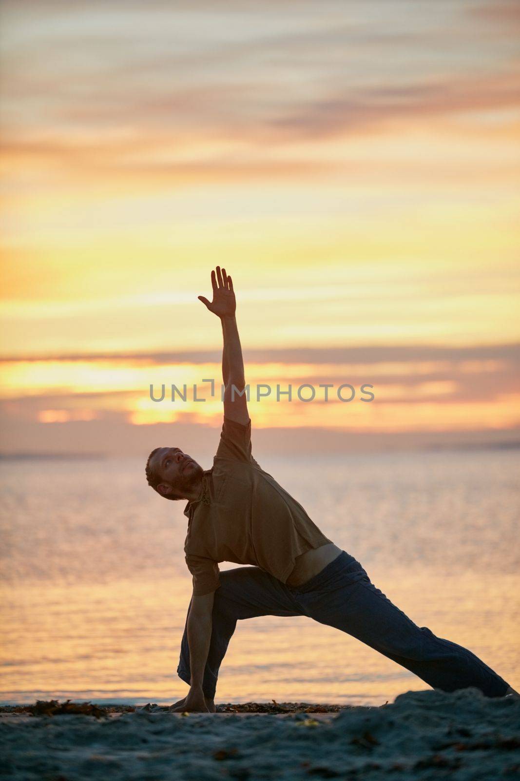 Yoga - bind the body and mind. a man practicing the triangle pose during his yoga routine at the beach. by YuriArcurs