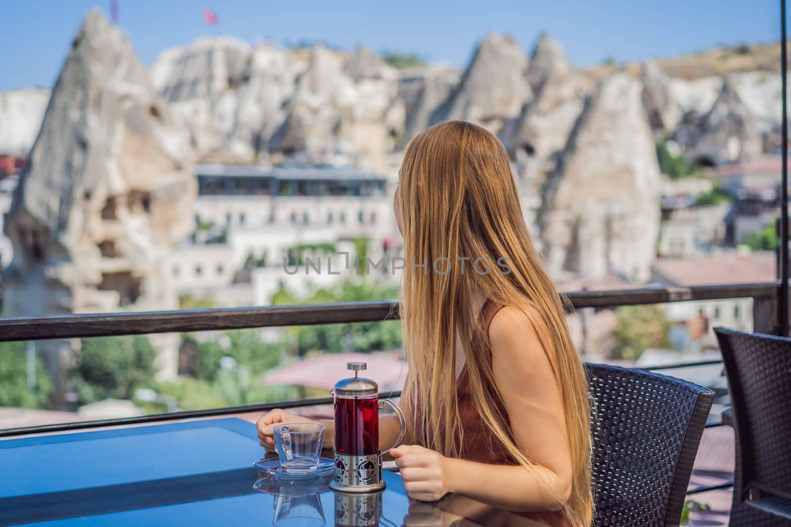 Young woman drinking coffee on the background valley with rock formations and fairy caves near Goreme in Cappadocia Turkey.