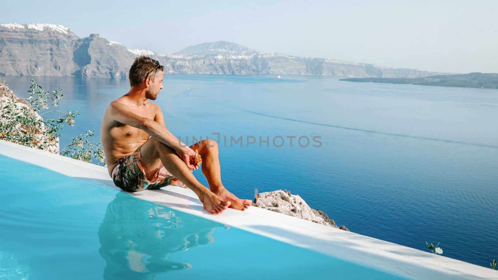 Santorini Greece Oia, young men in swim short in the pool looking out over the caldera ocean by fokkebok