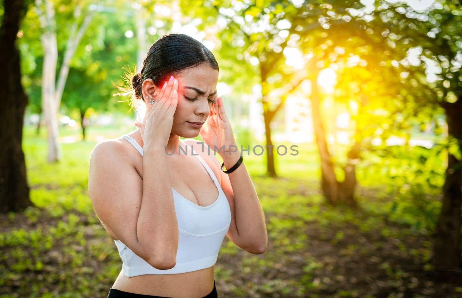 Young woman runner rubbing her head with migraine in a park. Runner woman with headache and fatigue in the park, Runner woman with headache in a park, Athlete girl with migraine in a park