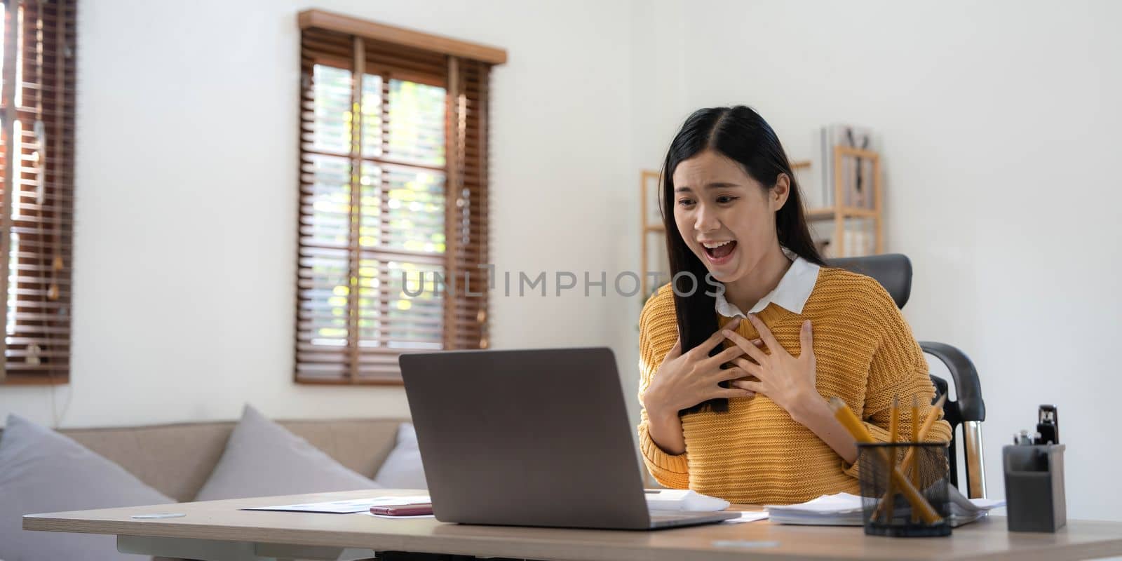 Excited happy woman looking at the laptop computer screen, celebrating an online win, overjoyed young asian female screaming with joy at home by wichayada
