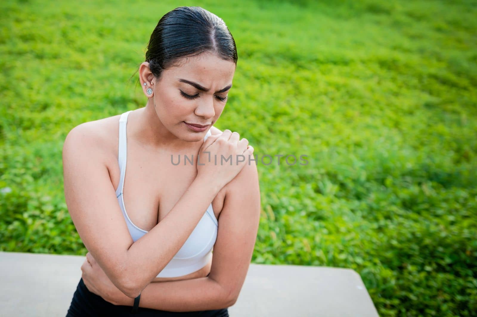 Girl suffering from shoulder pain sitting outdoors. Woman sitting and stressed with shoulder pain outdoors. Girl with shoulder pain outdoors, Young woman with shoulder pain sitting outside