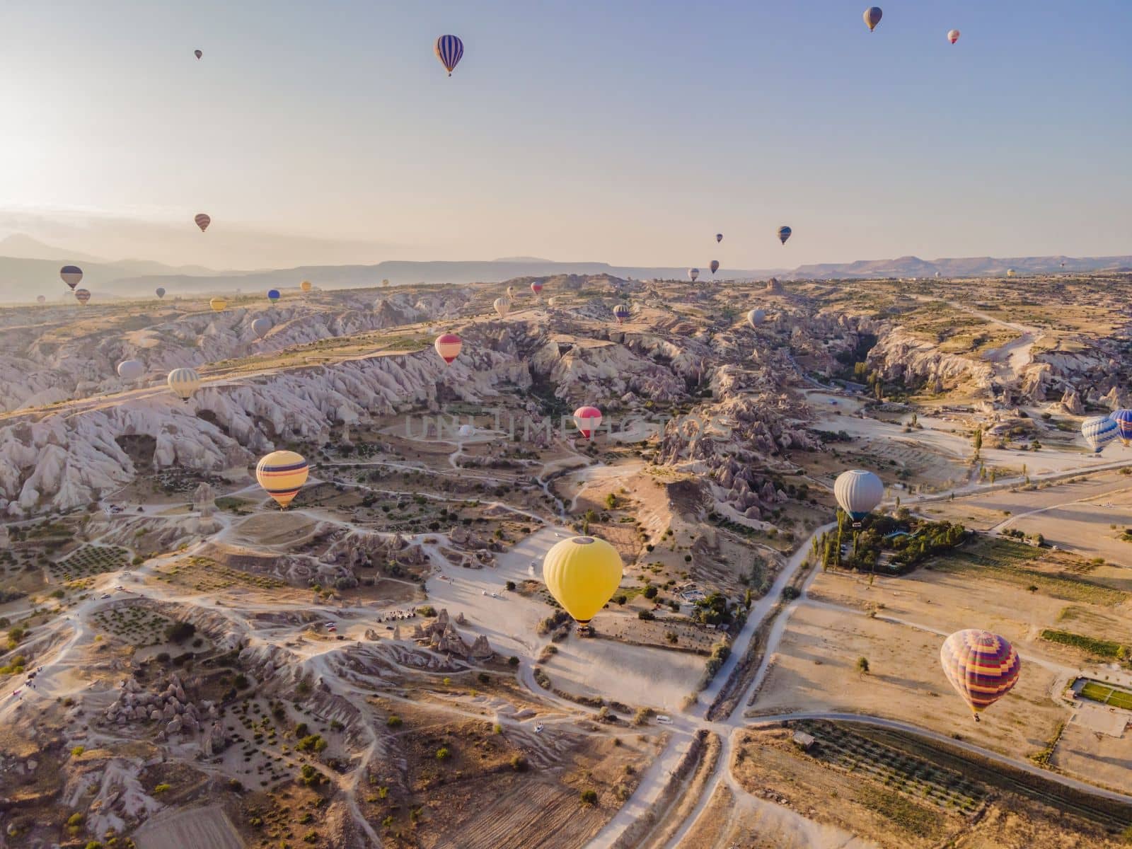 Colorful hot air balloons flying over at fairy chimneys valley in Nevsehir, Goreme, Cappadocia Turkey. Spectacular panoramic drone view of the underground city and ballooning tourism. High quality.