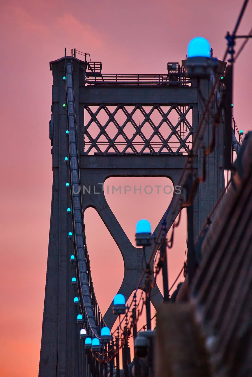 Blue lights in detail on support wires of American bridge with golden light behind by njproductions