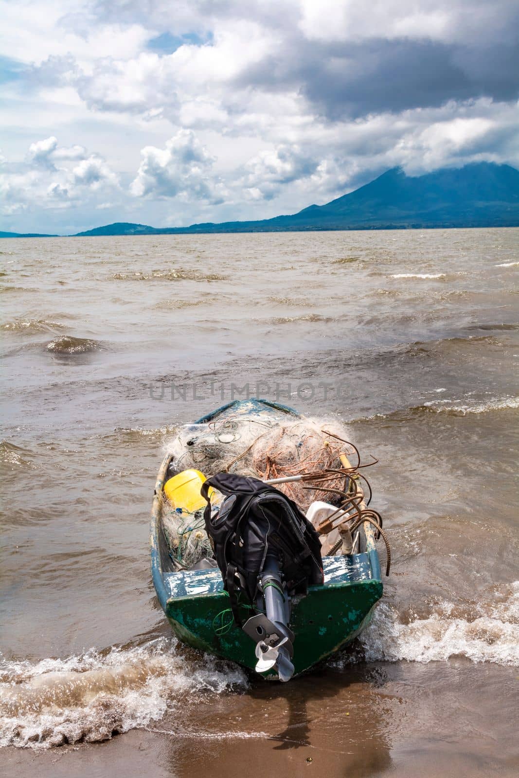 Fishing boat on the shore of a lake. A fishing boat on the shore of a lake with volcanoes in the background. A fishing boat on a lake in Nicaragua. Concept of fishing boats parked at the seaside by isaiphoto
