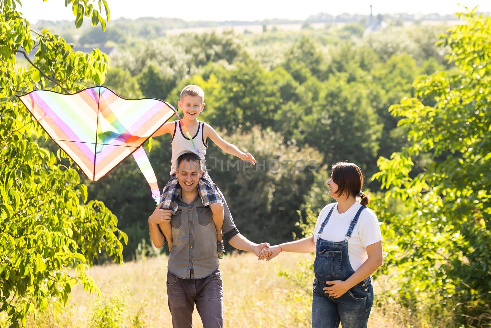 Happy family with pregnant wife fly a kite together in summer field