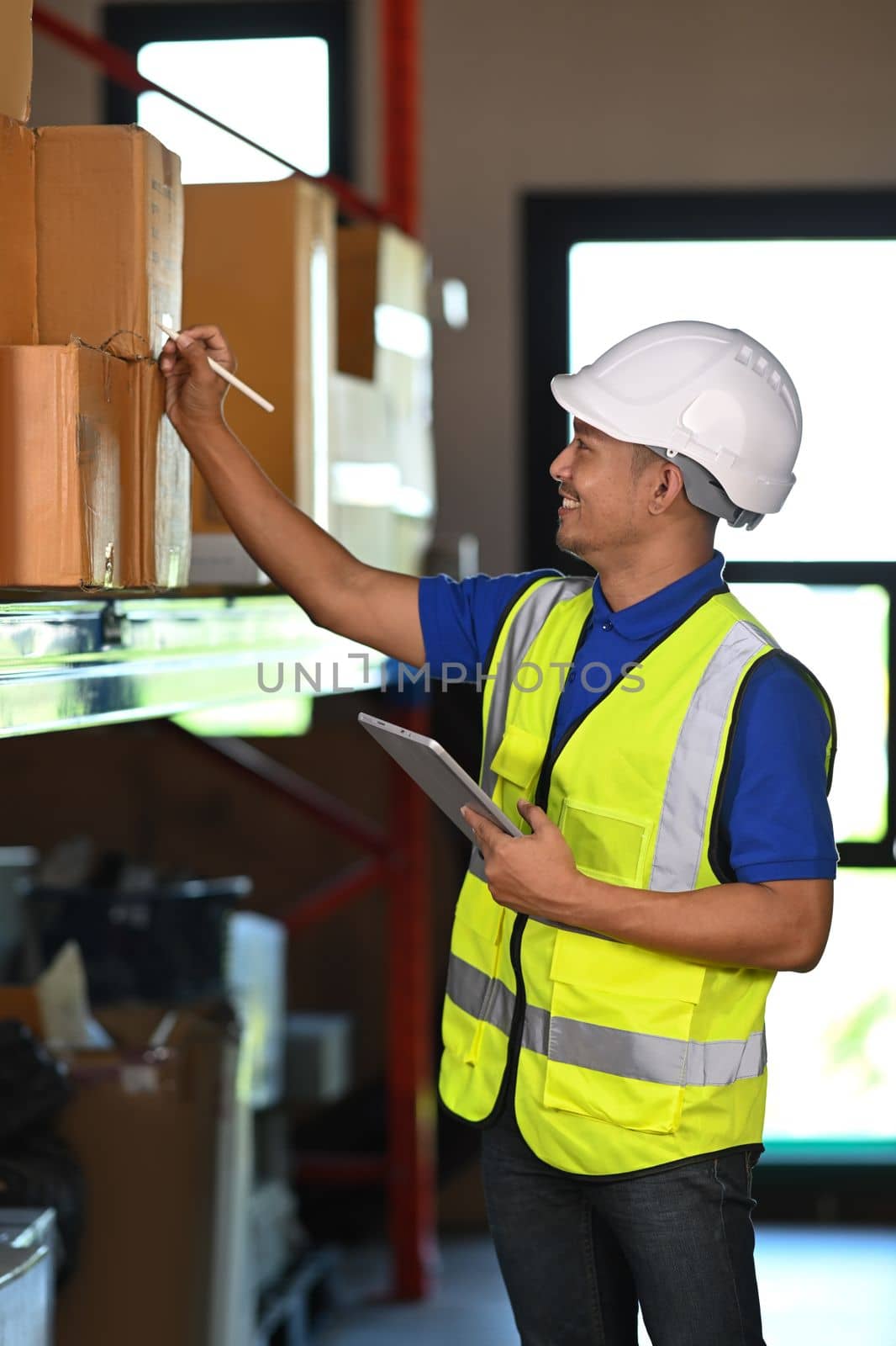 Warehouse worker checking order details on a tablet while standing between retail warehouse full of shelves.