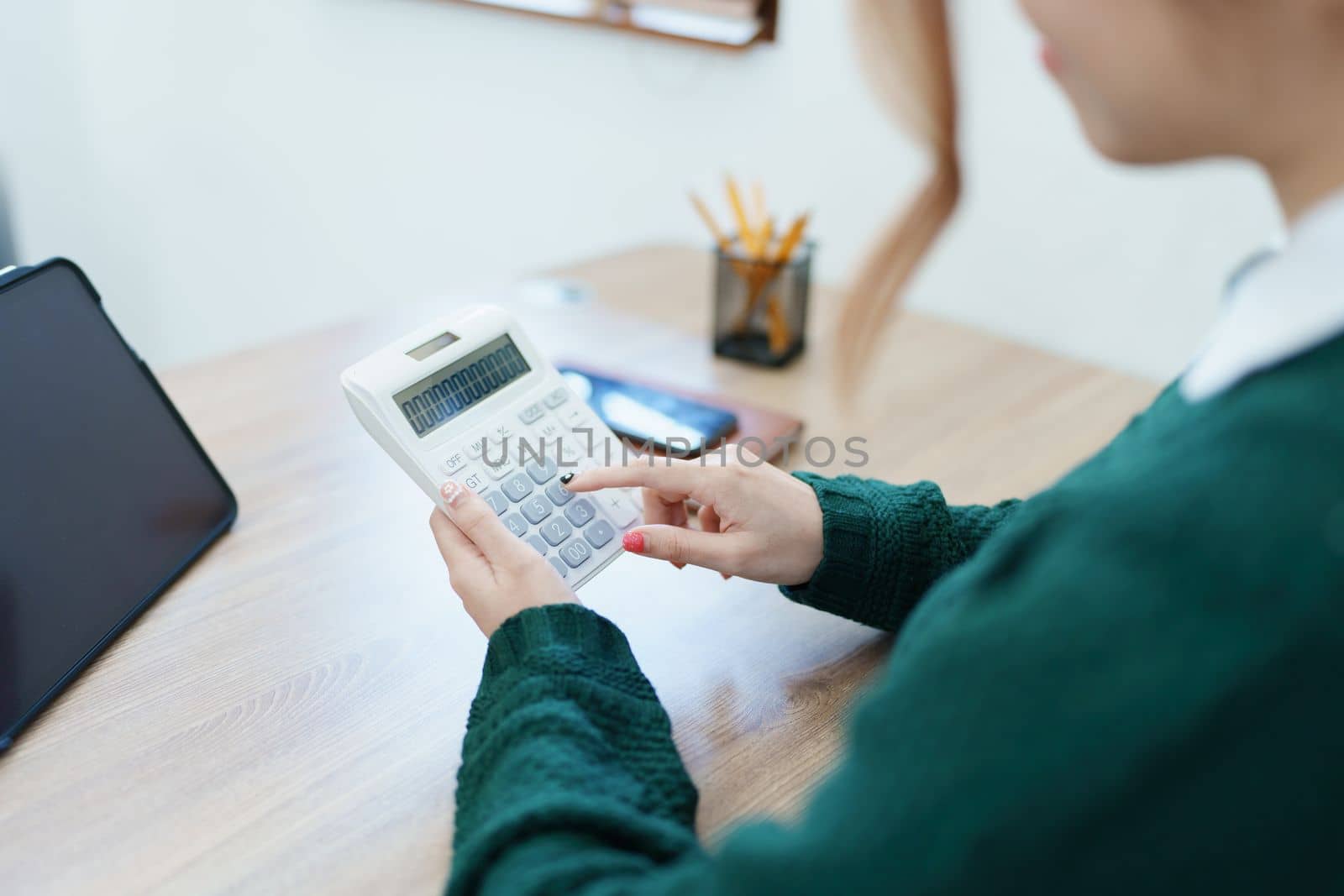 business owner or Asian female marketers are using calculator to calculate and tablet computer in office work by Manastrong