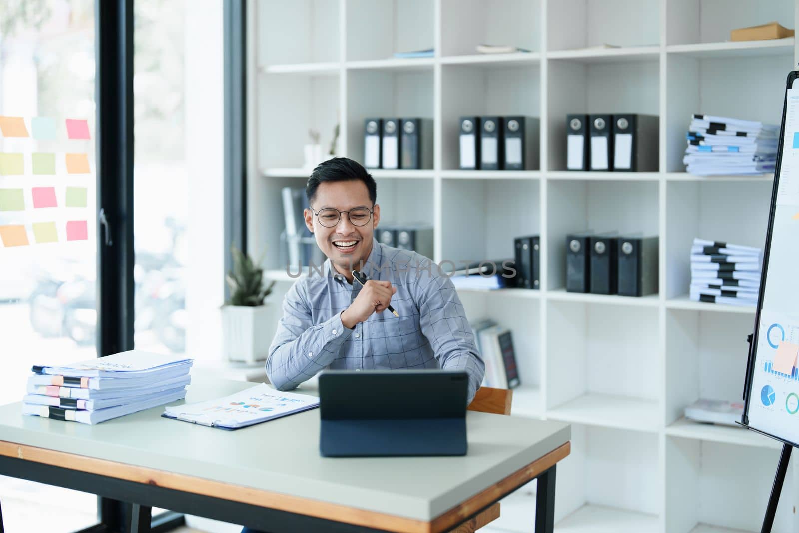 Portrait of a man business owner showing a happy smiling face as he has successfully invested her business using computers and financial budget documents at work by Manastrong
