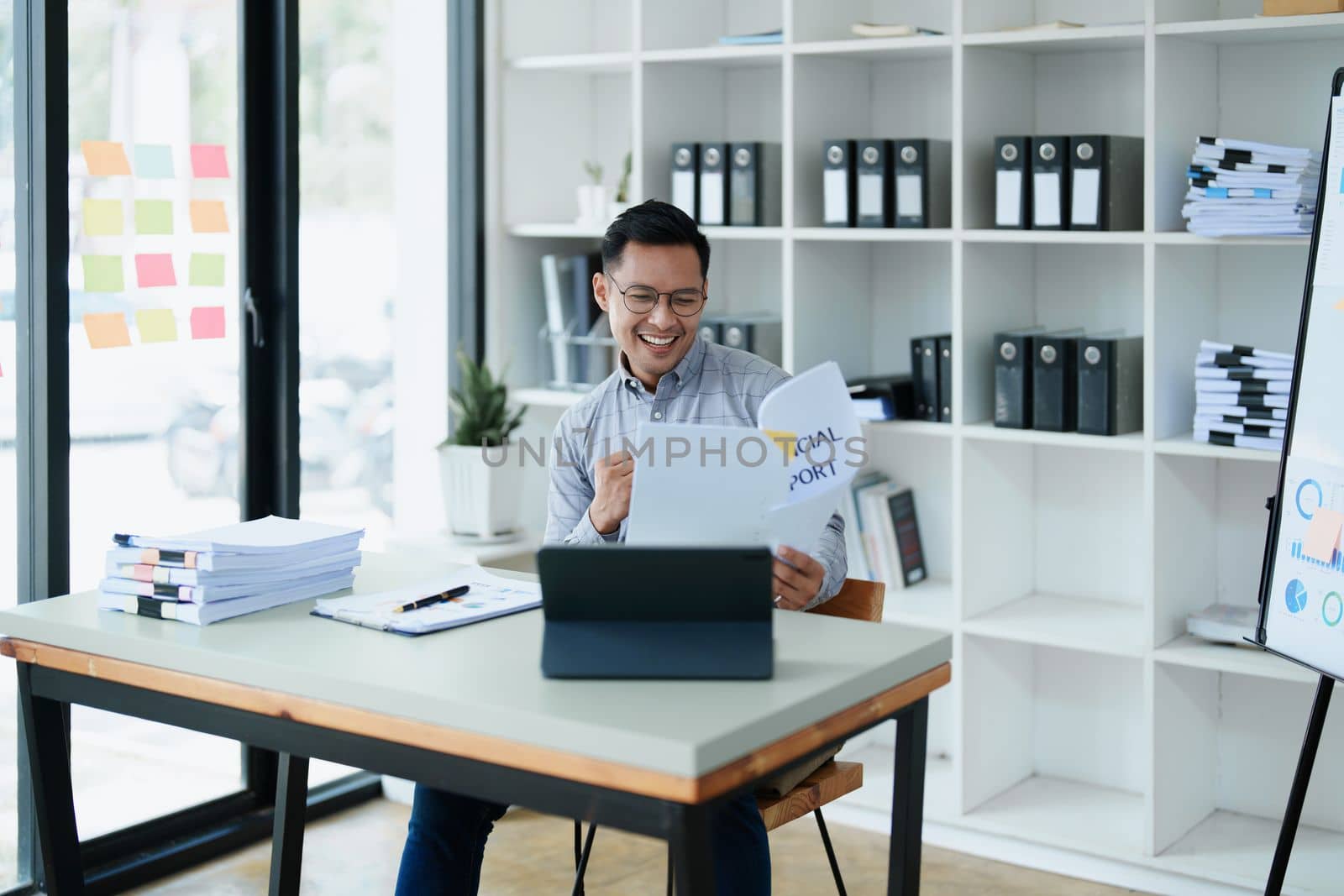 Portrait of a man business owner showing a happy smiling face as he has successfully invested her business using computers and financial budget documents at work.