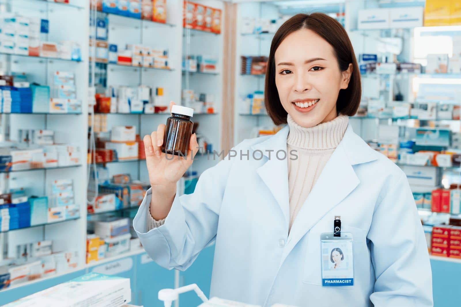 Portrait of young affable pharmacist show qualified medicine pill bottle mockup product for copyspace at pharmacy. Druggist working with her diary job at drugstore, medicine box on shelf at background