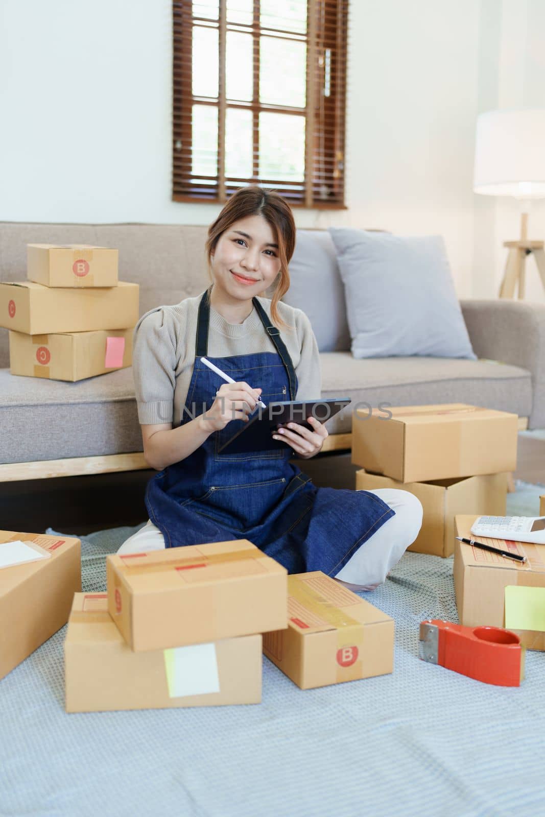 Starting small business entrepreneur of independent young Asian woman online seller is using smart phone and taking orders to pack products for delivery to customers. SME delivery concept.