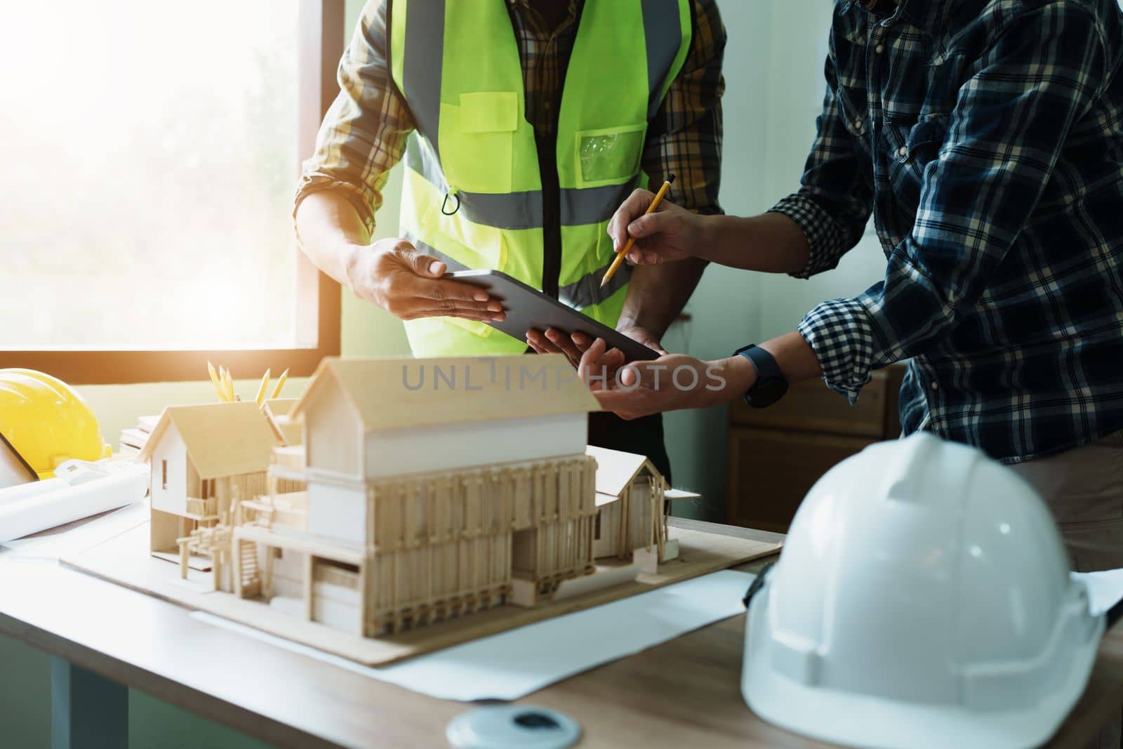 Engineers are consulting the team to design an architectural structure for clients with blueprints and building models to work at office.