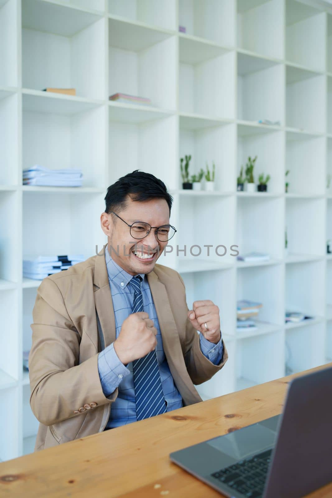 Portrait of an Asian male business owner standing with a computer showing happiness after a successful investment by Manastrong