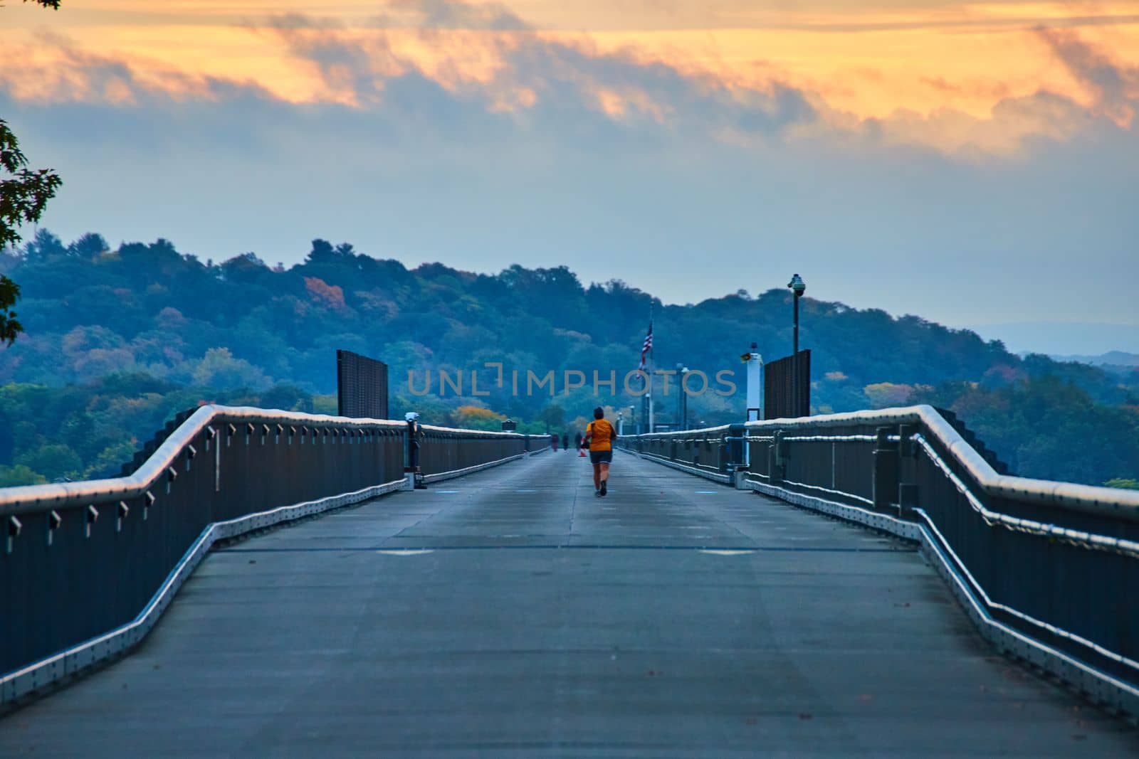 Image of Morning light over joggers on long straight cement bridge