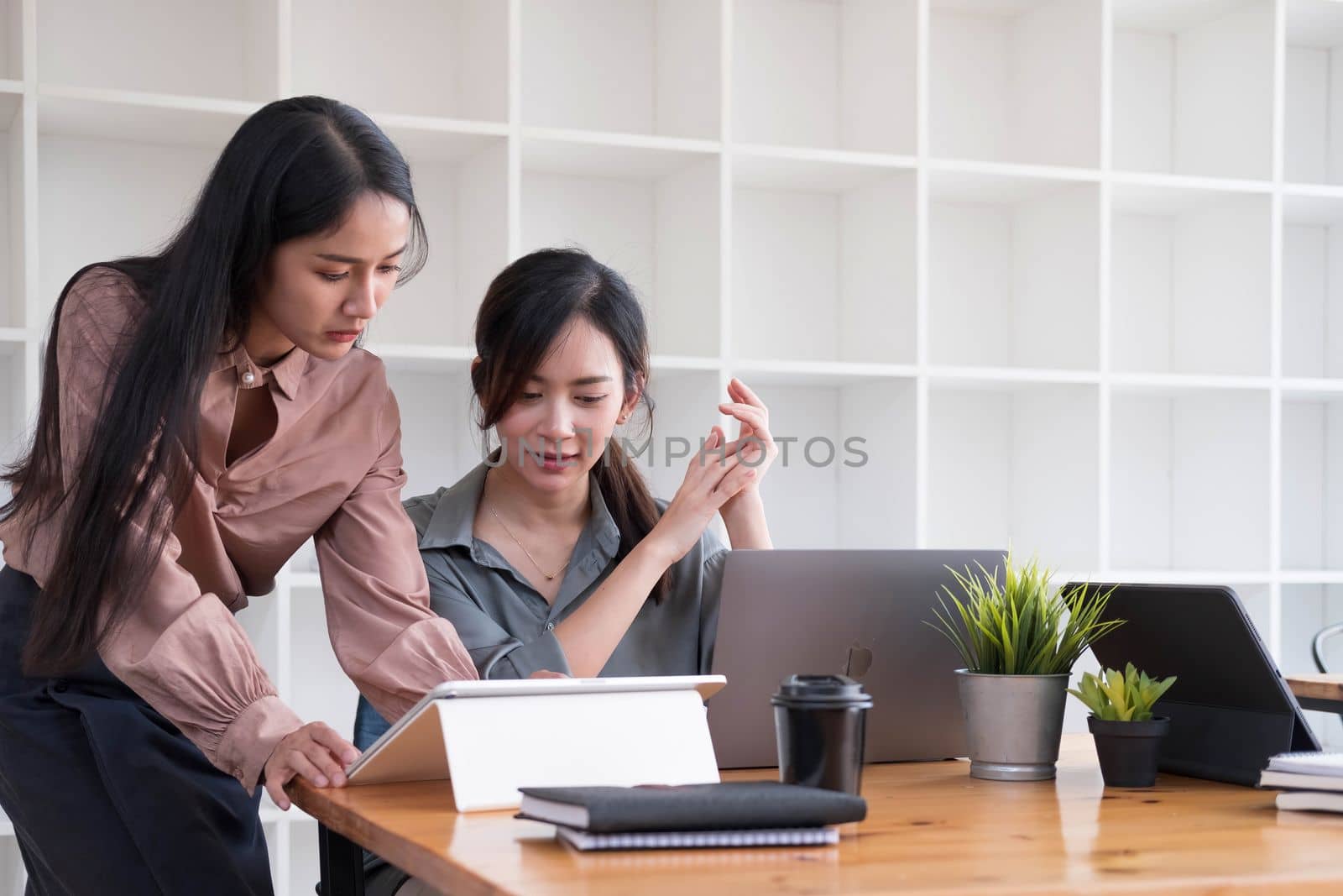 Two young Asian business woman talk, consult, discuss working with new startup project idea presentation analyze plan marketing and investment in the office. by wichayada