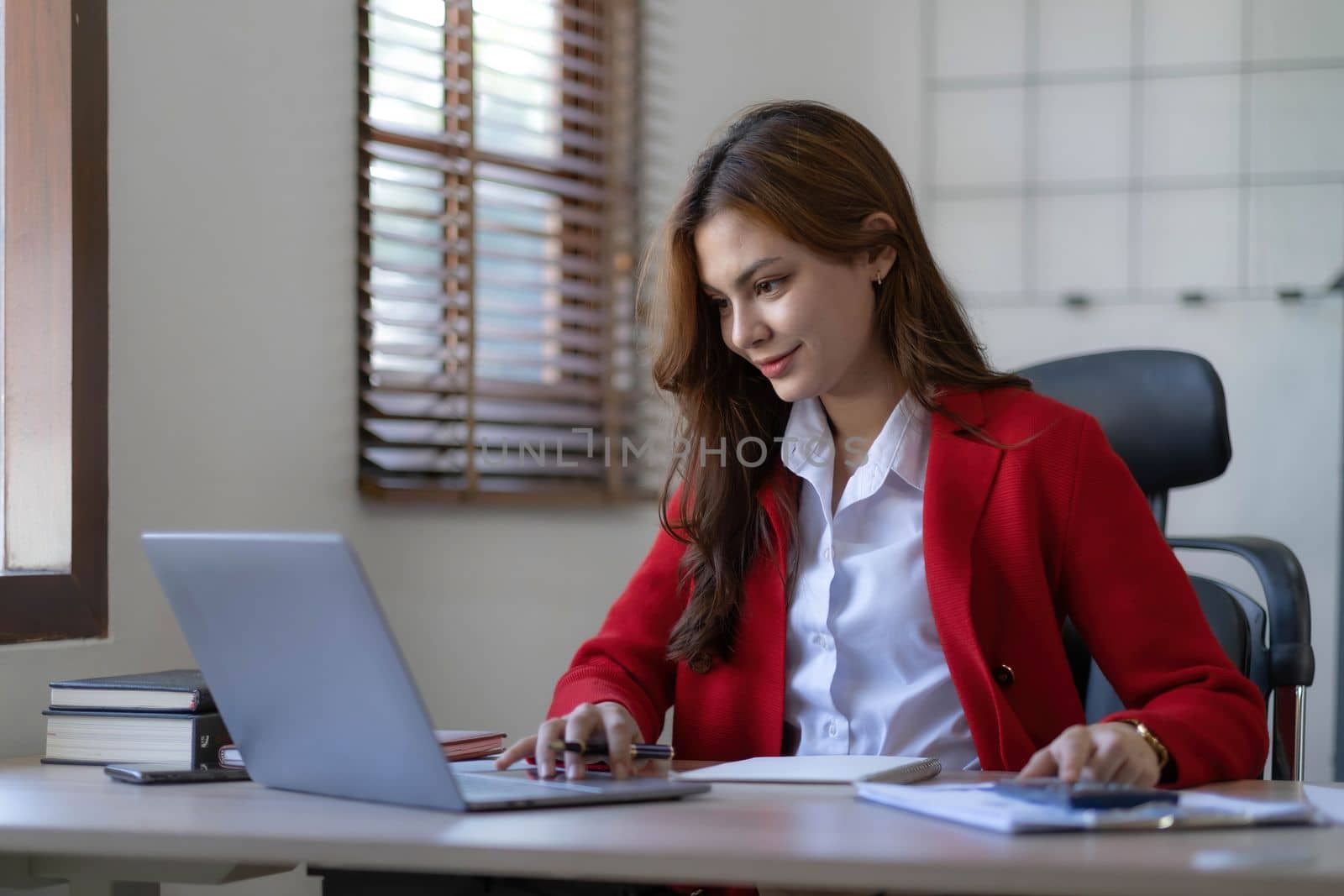 Asian Business woman using calculator and laptop for doing math finance on an office desk, tax, report, accounting, statistics, and analytical research concept..