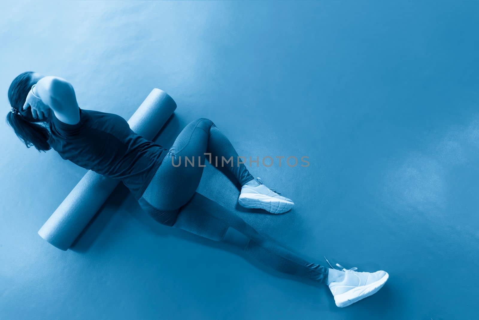 Woman doing foam roller exercise on a floor in gym by Mariakray