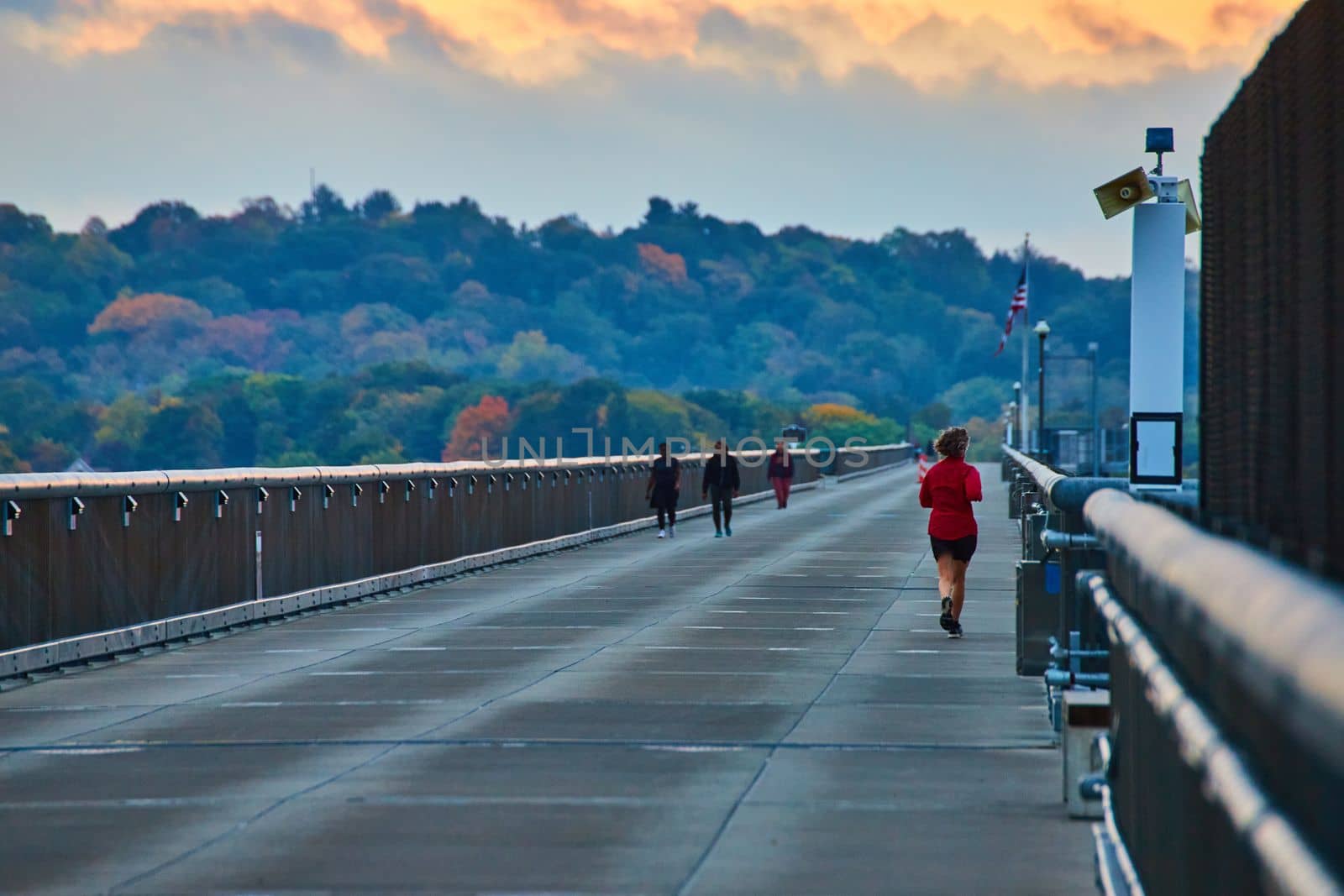 Joggers running along long cement bridge boardwalk with forests in background by njproductions