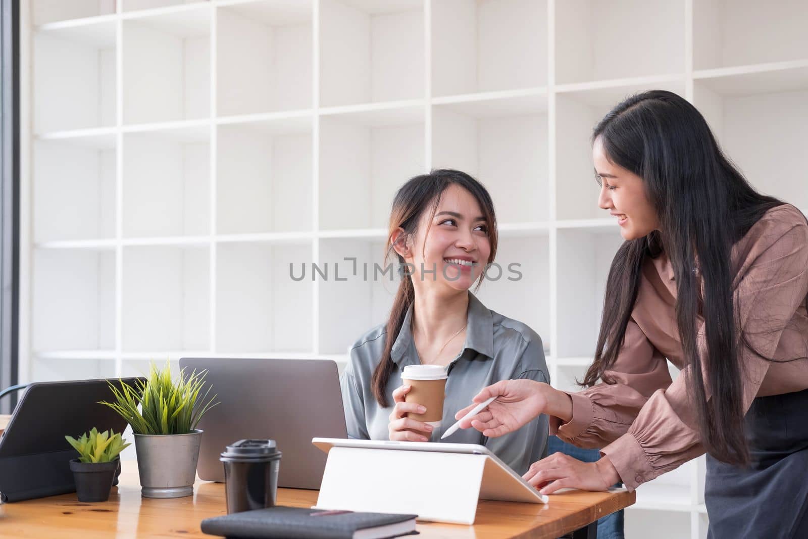 Two young Asian business woman talk, consult, discuss working with new startup project idea presentation analyze plan marketing and investment in the office...