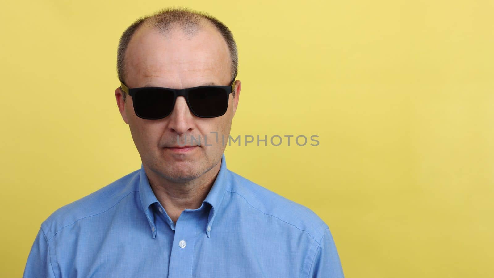 A man in black sunglasses on a yellow background.