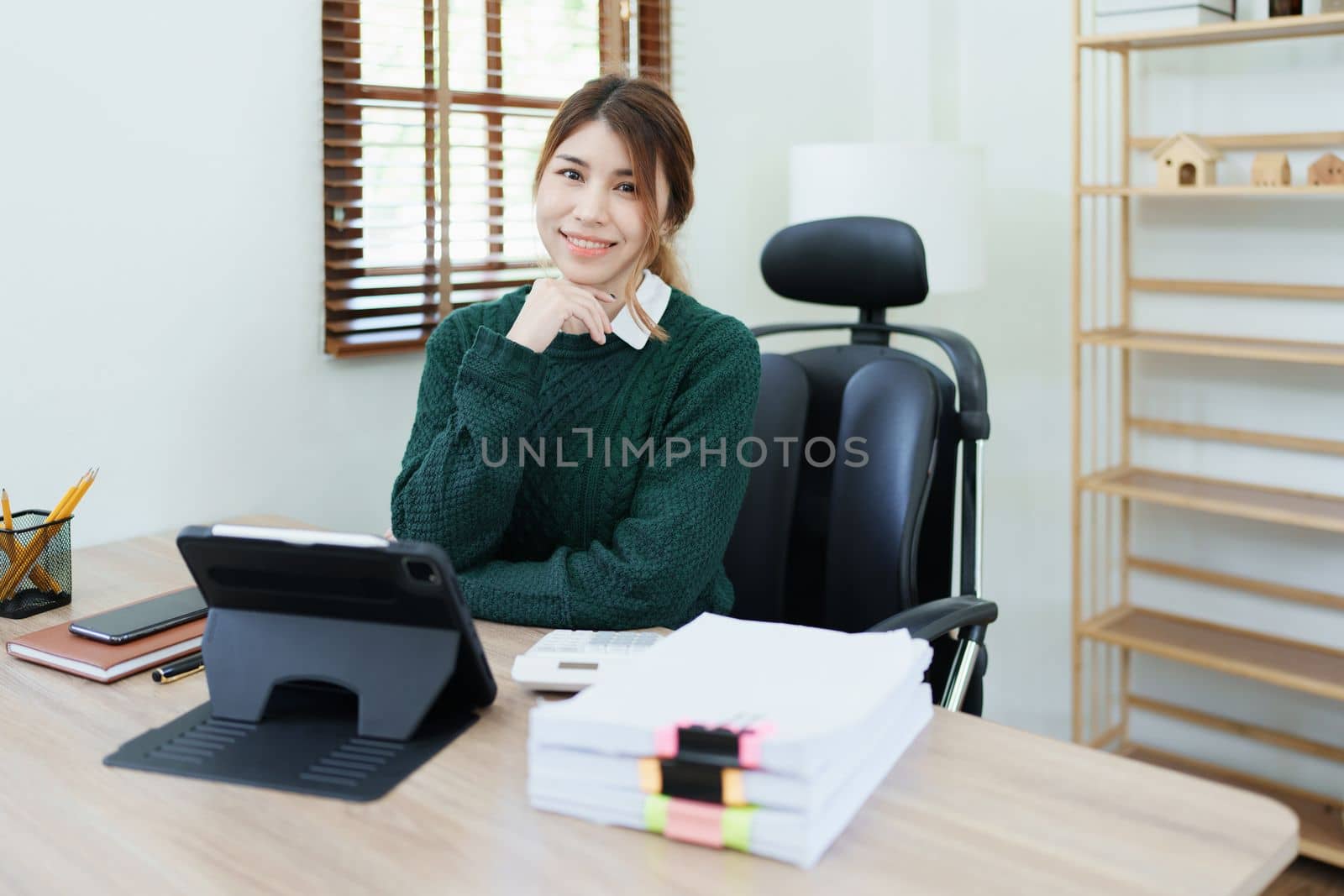 Portrait of a woman business owner showing a happy smiling face as he has successfully invested her business using computers and financial budget documents at work.