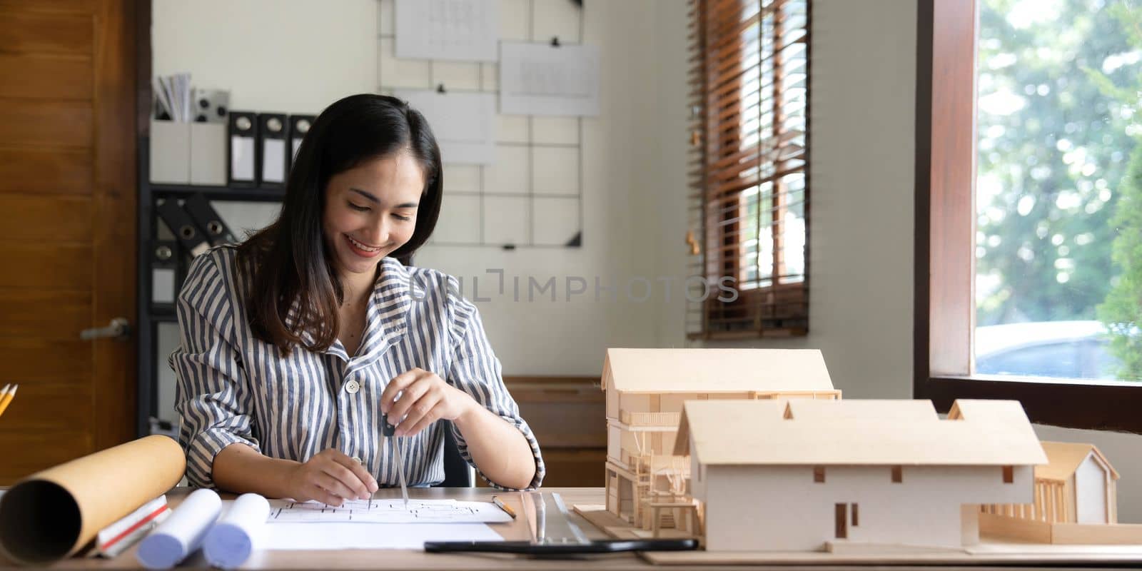 Architecture, building, construction and real estate concept - Happy smiling female architect with blueprint, ruler and living house model on table working at home office. Architect woman