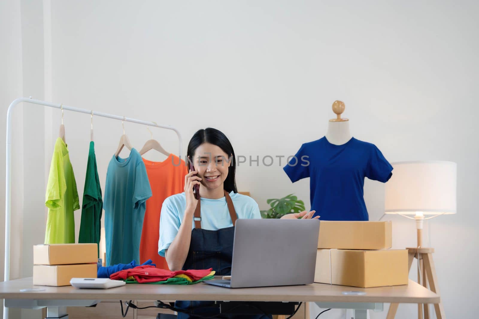 Beautiful asian woman online seller confirming orders from customer on the phone, Start small businesses SME owners female entrepreneurs use a laptop at home,pack and delivery situation concept..