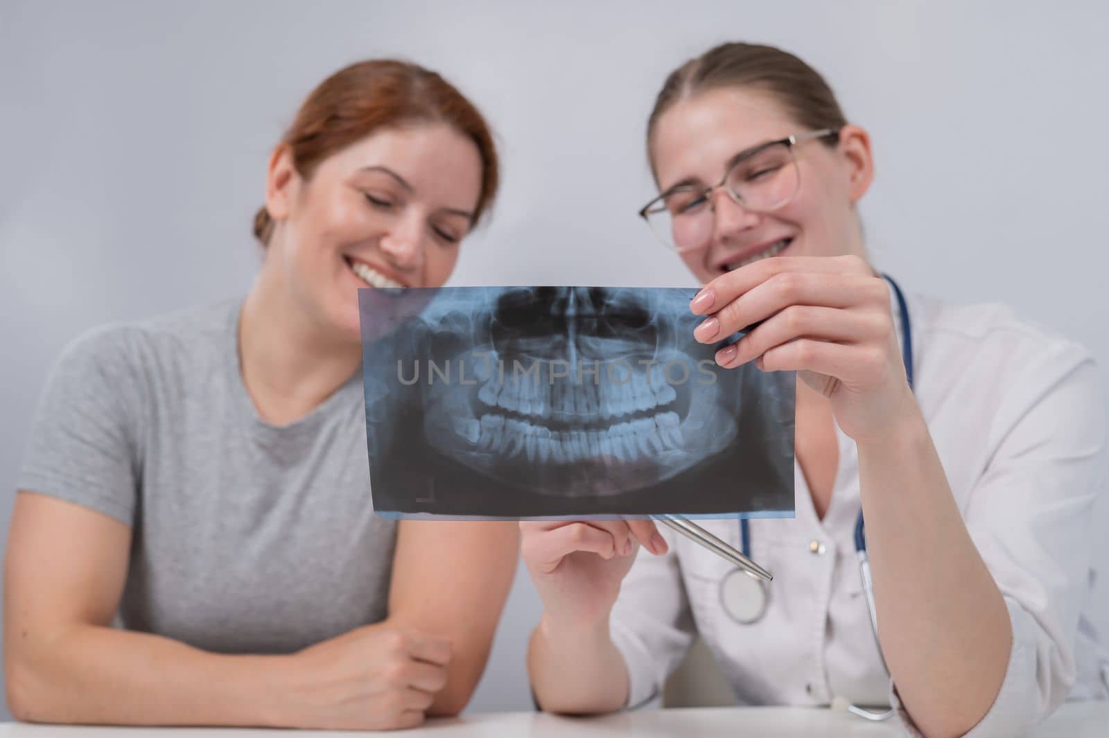 A woman doctor and a patient at the reception are discussing an x-ray of the jaw