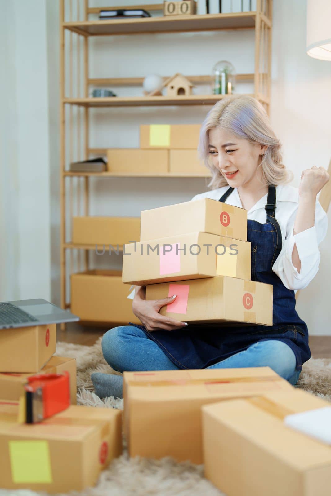 Starting small business entrepreneur of independent Asian woman smiling using computer laptop with cheerful success of online marketing package box items and SME delivery concept.