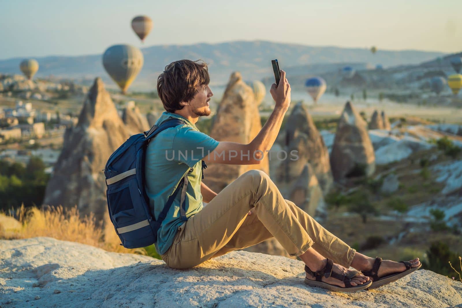 Tourist man looking at hot air balloons in Cappadocia, Turkey. Happy Travel in Turkey concept. Man on a mountain top enjoying wonderful view.