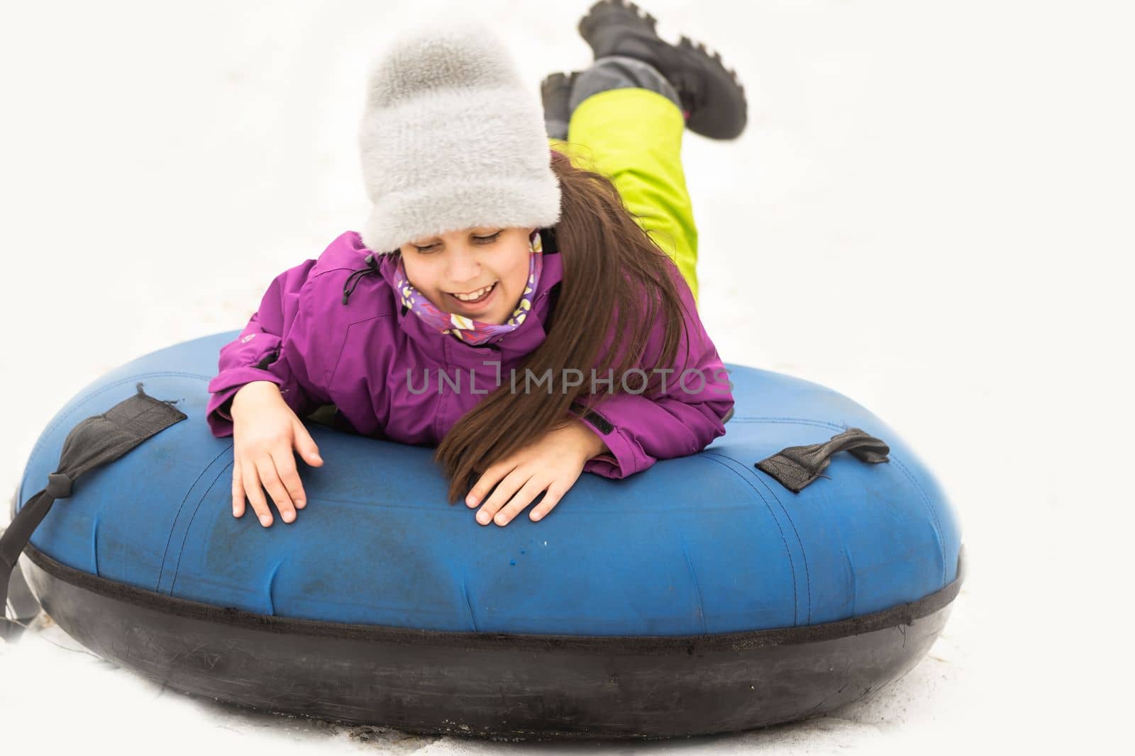 Active girl sliding down the hill on snow tube. Cute little happy child having fun outdoors in winter on sledge . Healthy excited kid tubing snowy downhill, family winter time.