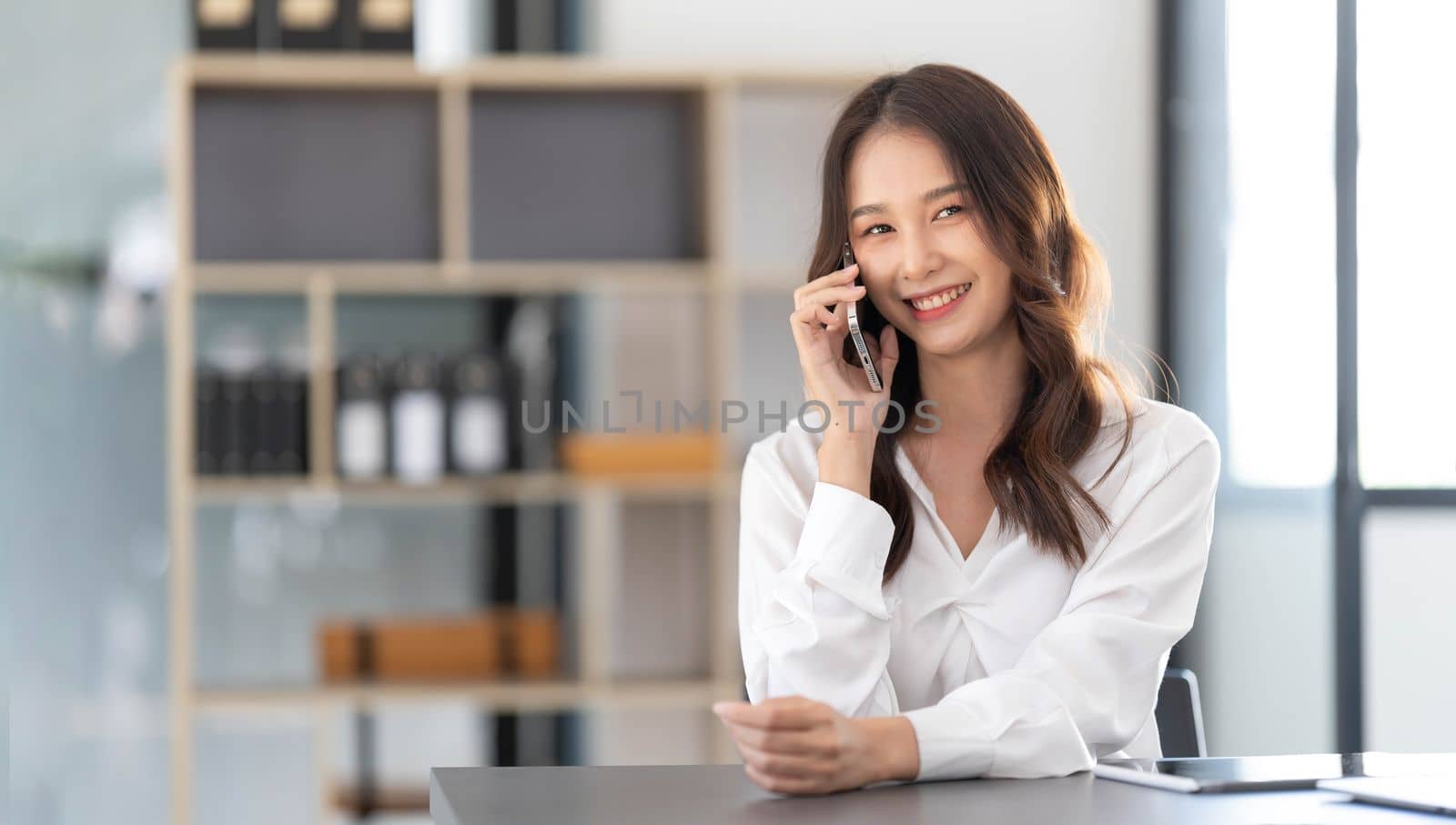 Young Asian businesswoman sit with her laptop computer happily talking on the phone with her customer explaining the detail in the office...