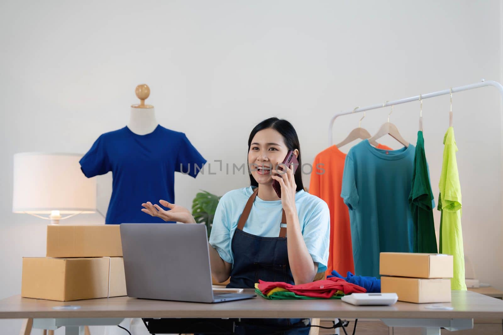 Beautiful asian woman online seller confirming orders from customer on the phone, Start small businesses SME owners female entrepreneurs use a laptop at home,pack and delivery situation concept..
