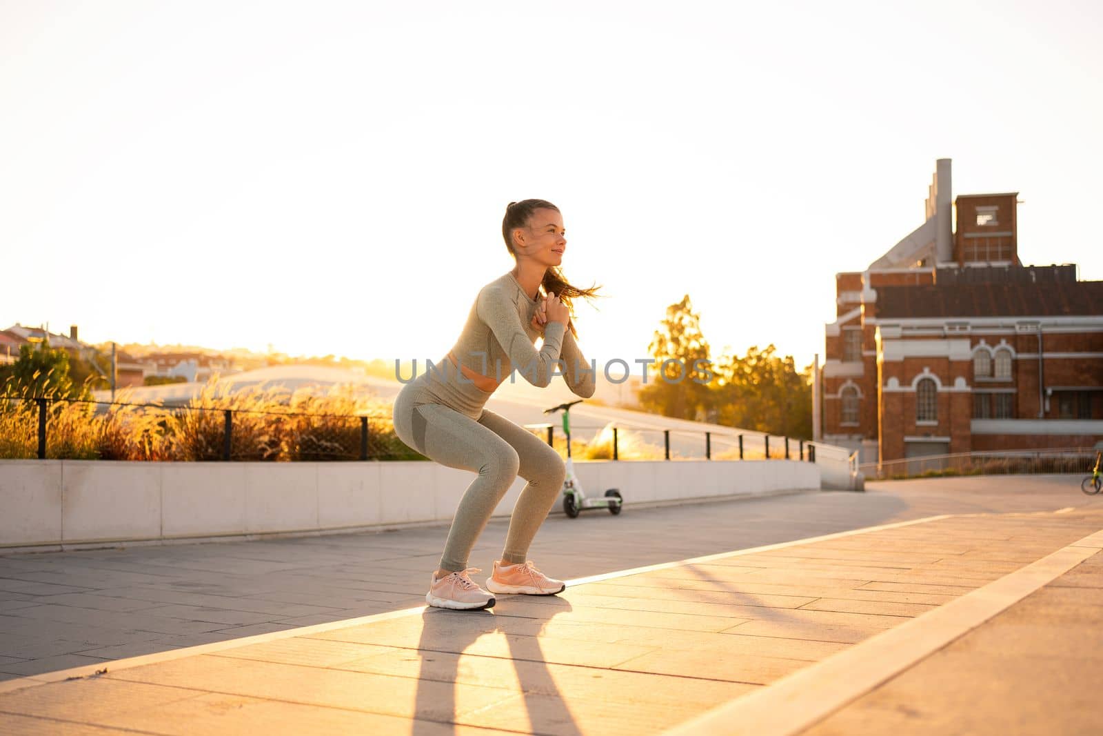 Sporty woman doing jumping squats exercises on stairs in park. Bodyweight training on sunset. Young adult fitness woman exercising outdoor. European woman squats. Athletic caucasian female workout