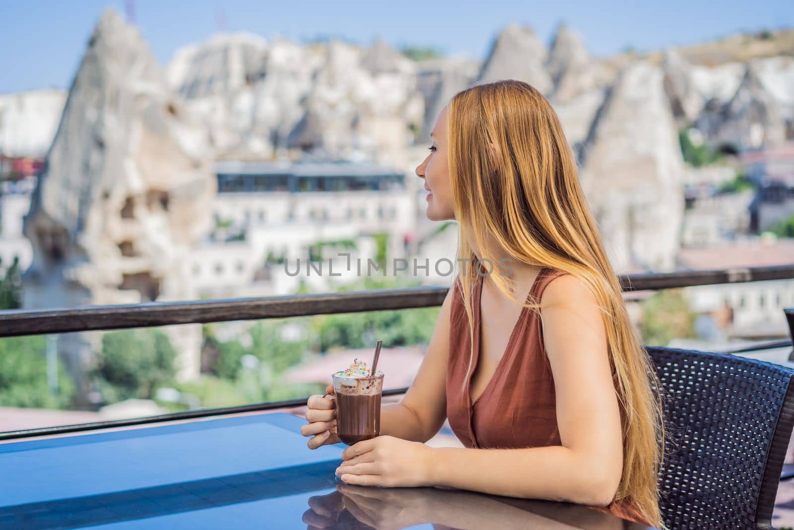 Young woman drinking coffee on the background valley with rock formations and fairy caves near Goreme in Cappadocia Turkey.