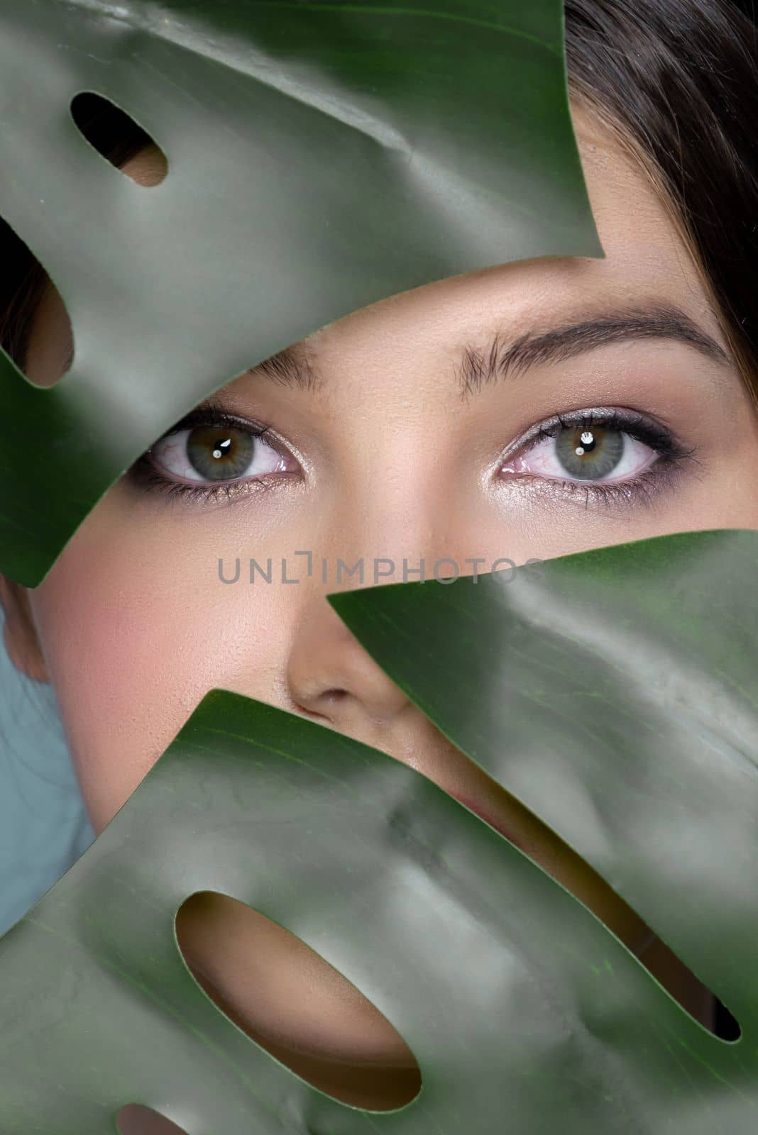 Portrait of young woman face surrounded with tropical green leaves. Healthy clean and perfect smooth skin of charming young woman. Natural beauty cosmetic and wellness concept for skincare product.
